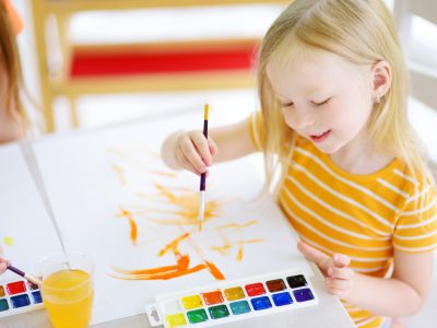 Cute little girl drawing with colorful paints at a daycare. Creative kid painting at school. Girl doing homework at home.